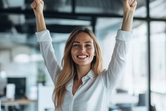 A woman is smiling and holding her hands up in the air. She is wearing a white shirt and has long hair. Concept of happiness and positivity