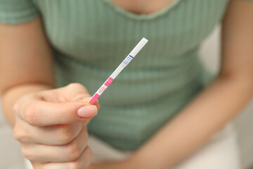 Woman holding pregnancy test indoors, closeup view © New Africa
