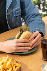 Woman eats delicious hamburger with french fries at table