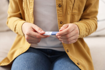 Woman holding pregnancy test on sofa indoors, closeup