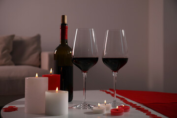 Burning candles, wine and paper hearts on table indoors