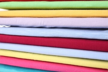 Stack of clean colorful t-shirts as background, closeup