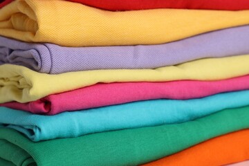 Stack of clean colorful t-shirts as background, closeup