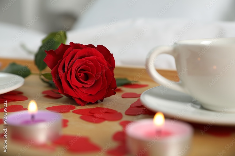 Poster Wooden tray with burning candles, rose, cup of drink and red paper hearts on bed indoors, closeup