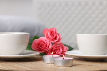 Burning candles, two cups of drink and flowers on wooden table indoors, closeup