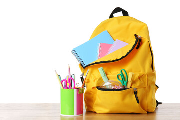 Backpack with different school stationery on wooden table against white background, space for text