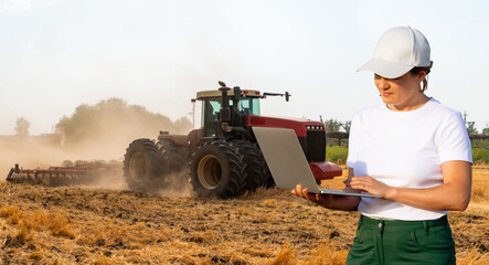 Female farmer with laptop controls an autonomous tractor on a smart farm