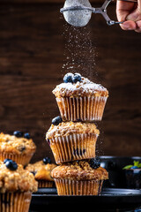 Blueberry muffins placed one on top of the other are sprinkled with powdered sugar on top