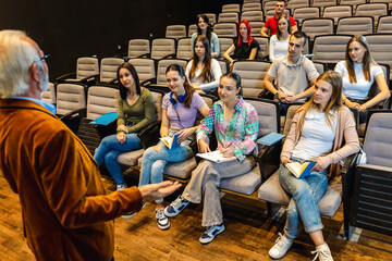 Male elderly professor lecturing students in amphitheater.