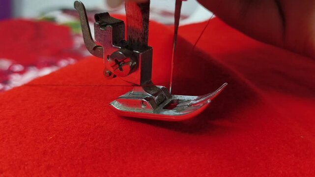 Tailor hand lowering professional clothing accessory electric sewing machine stitching hem tool and needle on red fabric. Tailoring or textile industry machinery concept. Close up macro side view.