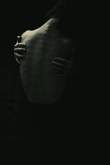 In the darkness, the thin figure of a sad young woman is visible, hugging herself in despair. Loneliness and depression hang heavily over her.