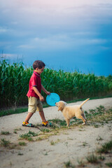 Handsome little boy playing frisbee with his beloved golden retriever puppy dog on countryside...