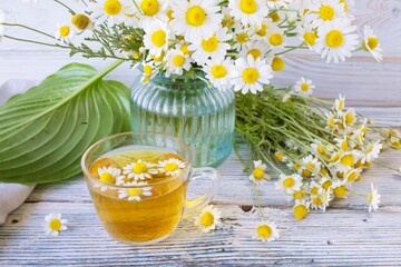 Herbal medicinal tea with chamomile flowers in a glass cup, a bouquet of fresh flowers, on a wooden...