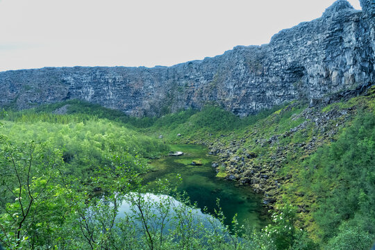 Botnstjörn pond surrounded by basalt cliffs and green trees