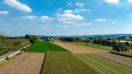 Expansive farmland showcases a patchwork of green and golden fields under a bright sky with scattered clouds.