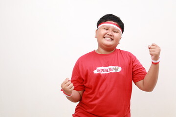 Fototapeta premium Young Asian boy with positive expression, joyful and exciting, dressed in casual cloth and red white ribbon over white background. Happy adorable glad boy rejoices success. Independence day concept