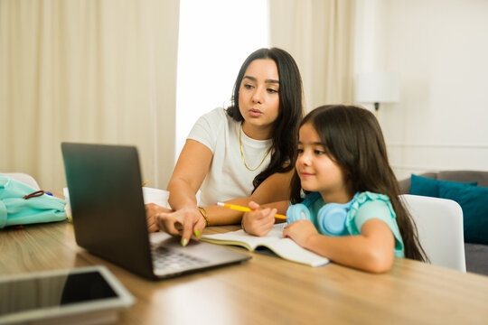 Hispanic woman homeschooling her daughter using a laptop at their dining room table