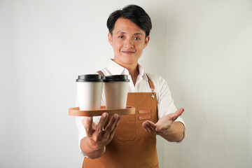 Excited young asian man wearing rolled-up white sleeve shirt and brown apron is holding and serving...