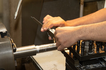 Close up scene the machine operator measuring dimension of metal shaft parts by Vernier caliper on lathe machine.