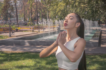 Fototapeta premium Asian girl holding her hands in namaste and doing yoga breathing exercises in the park. Meditation. Healthy lifestyle