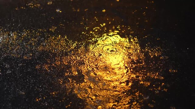 Raindrops fall on a wet night street.
Night street in rainy weather.
Puddle during the rain.
Street lights illuminate the street at night during the rain