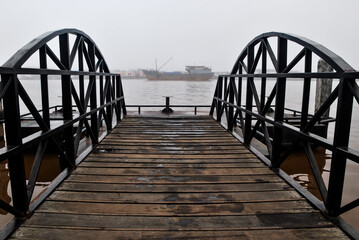 A foggy morning reveals a rustic wooden bridge leading to a serene waterfront