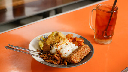 Nasi rames with fried tempeh, balado potatoes and tempeh orek. Nasi rames is a typical Indonesian food in the form of rice with side dishes, accompanied by a glass of fresh iced tea