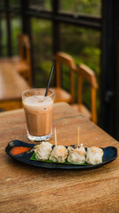 Dimsum, a typical Japanese food, is arranged on an oval plate with separate chili sauce and served with a glass of coffee with palm sugar milk
