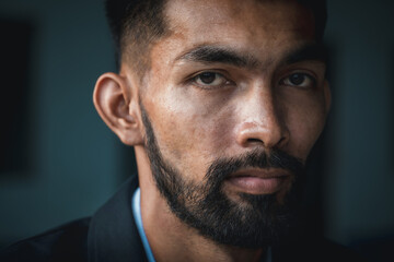 Close-up of young man's face with a beard and mustache in a black studio, background and looking at camera