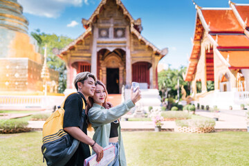 smiling tourist lover taking phone selfie at asia temple. happy asian lover using smartphone taking photo while on vacation. young cheerful asian couple at asia ancient temple using phone to selfie