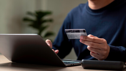 A man is using a laptop to pay for something with a credit card. Concept of convenience and modernity, as the man is able to complete a transaction using a digital device