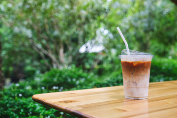 A glass of iced latte coffee on wooden table in the garden