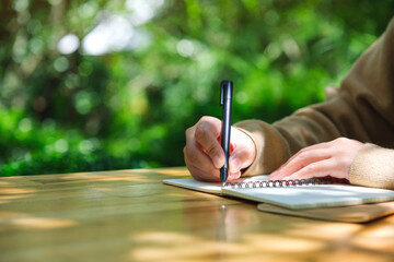 Closeup image of a woman writing on a notebook in the outdoors
