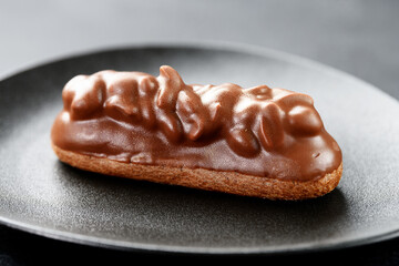 Beautiful french eclair with chocolate and nuts filling  on a black plate