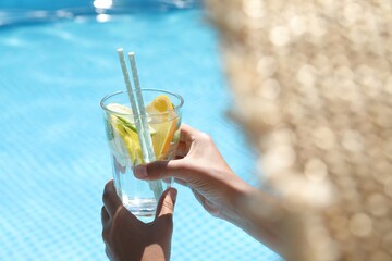 Woman holding tasty cocktail in glass near swimming pool outdoors, closeup