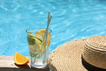 Tasty cocktail in glass and straw hat near swimming pool outdoors