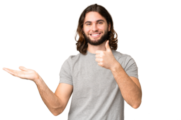 Young handsome man over isolated chroma key background holding copyspace imaginary on the palm to insert an ad and with thumbs up
