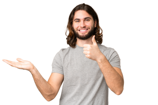 Young handsome man over isolated chroma key background holding copyspace imaginary on the palm to insert an ad and with thumbs up