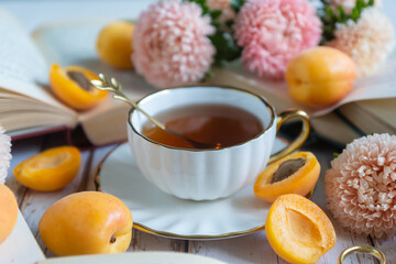 A cup of tea, ripe apricots and cakes on the table, aster flowers. August.