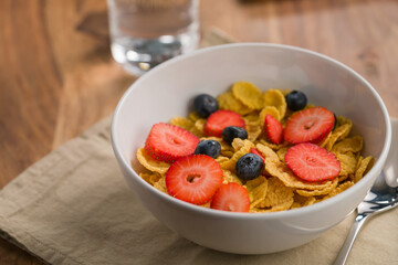 corn flakes with berries in white bowl for breakfast on table