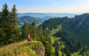 pretty senior woman hiking in warm dawn sunlight and enjoying the spectacular view over the Allgau alps on the Nagelfluh mountain chain near Oberstaufen, Bavaria, Germany