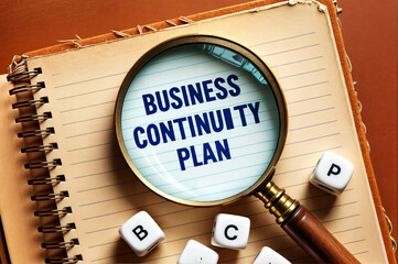 A magnifying glass over a notebook with the word text "BCP" acronym abbreviation of Business Continuity Plan, suggesting a focus on business preparedness.