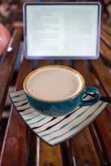 A coffee cup sits on a striped saucer against a digital tablet background in a cozy cafe