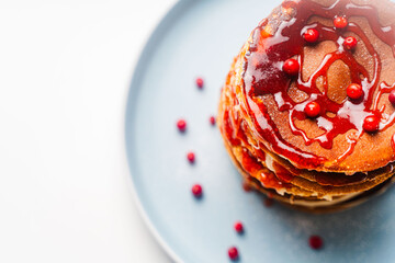A stack of traditional American pancakes with raspberry and lingonberry sauce with berries on a blue plate on a white table. Copyspace