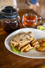 Enjoy a delectable sandwich accompanied by crispy fries and a cup of tea on a rustic wooden table