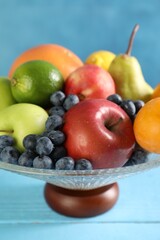 Glass vase with different fresh fruits on light blue wooden table, closeup