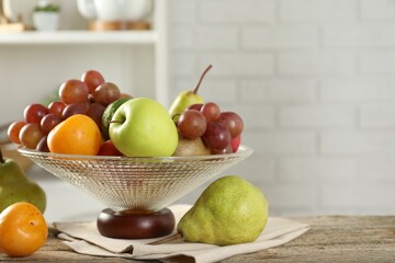 Glass vase with different fresh fruits on wooden table. Space for text