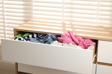 Cluttered chest of drawers indoors. Clothes in mess