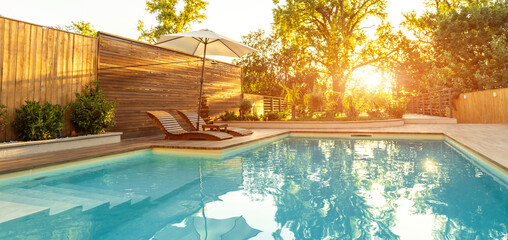 Panorama of luxury swimming pool in Modern Villa with Palm Trees and wooden lounge chairs at sunset