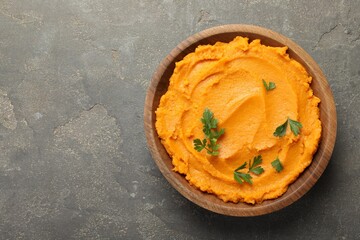 Delicious mashed sweet potatoes with parsley in bowl on gray textured table, top view. Space for text
